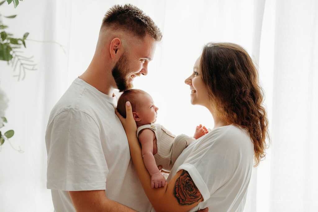 mama w jasnej sukience trzyma noworodka podczas sesji noworodkowej