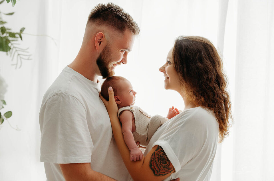 mama w jasnej sukience trzyma noworodka podczas sesji noworodkowej