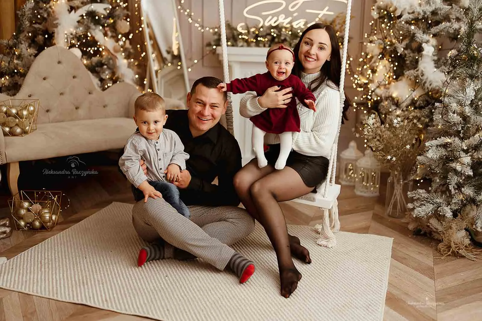 Rodzinne zdjęcie świąteczne – mama z niemowlakiem na huśtawce, tata z synem obok, świąteczna aranżacja studio Noworodkowo Warszawa